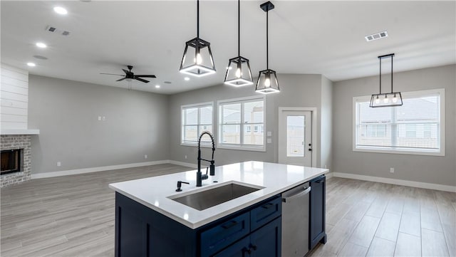 kitchen featuring pendant lighting, sink, stainless steel dishwasher, blue cabinetry, and a center island with sink