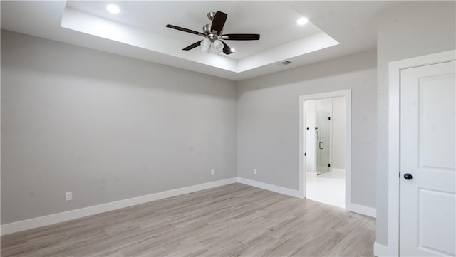 empty room with ceiling fan, a raised ceiling, and light hardwood / wood-style flooring