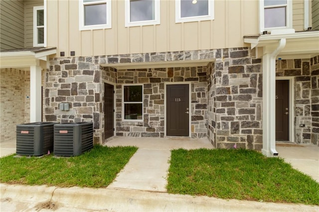 doorway to property with central air condition unit, stone siding, and board and batten siding