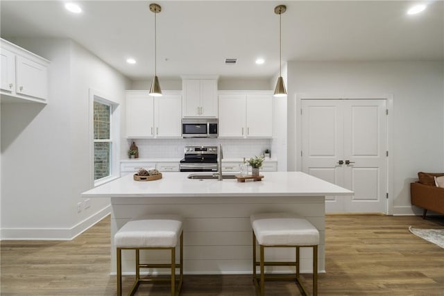 kitchen with wood finished floors, backsplash, a kitchen bar, baseboards, and appliances with stainless steel finishes