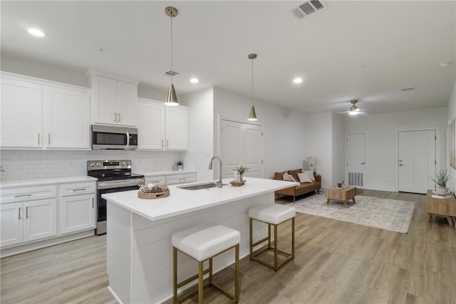 kitchen featuring visible vents, a sink, light wood-style floors, tasteful backsplash, and appliances with stainless steel finishes