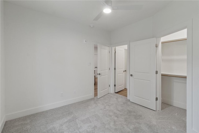 unfurnished bedroom featuring a walk in closet, baseboards, a ceiling fan, and carpet floors