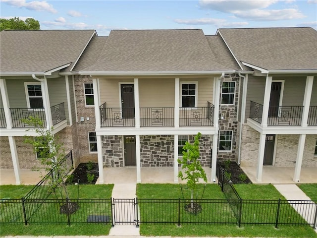 exterior space with stone siding, a gate, a lawn, a balcony, and a fenced front yard