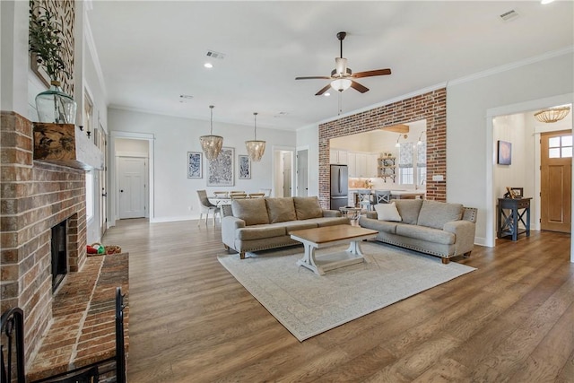 living room featuring a fireplace, wood-type flooring, ceiling fan with notable chandelier, and ornamental molding