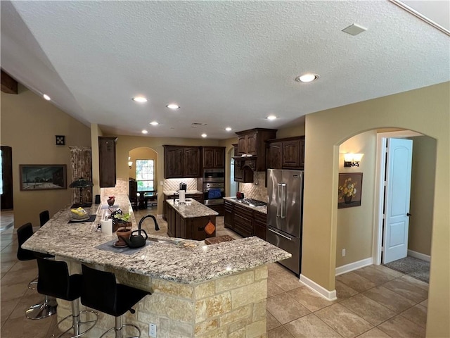 1142 Fletcher, Anderson, TX 77830 - kitchen with arched walkways, stainless steel appliances, dark brown cabinetry, tasteful backsplash, and a peninsula
