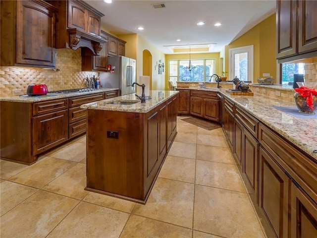 1142 Fletcher, Anderson, TX 77830 - kitchen with stainless steel appliances, decorative backsplash, light stone countertops, light tile patterned flooring, and a center island with sink