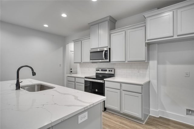 kitchen with light stone countertops, appliances with stainless steel finishes, decorative backsplash, sink, and light hardwood / wood-style floors