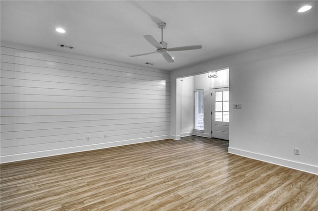 unfurnished room featuring ceiling fan, wooden walls, and light hardwood / wood-style floors