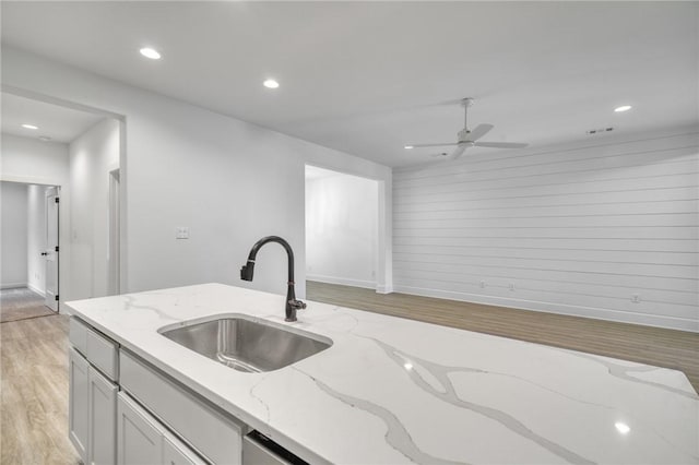 kitchen with light stone countertops, light wood-type flooring, ceiling fan, sink, and white cabinets