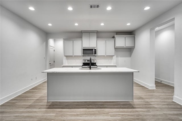 kitchen featuring light hardwood / wood-style floors, sink, stainless steel appliances, and an island with sink