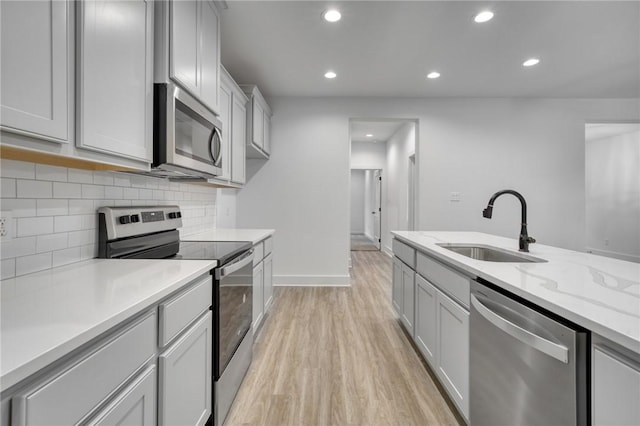 kitchen with sink, light stone counters, backsplash, light hardwood / wood-style floors, and appliances with stainless steel finishes