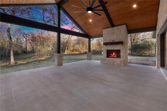 patio terrace at dusk with ceiling fan and an outdoor stone fireplace