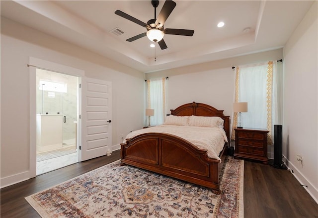 bedroom with ceiling fan, dark wood-type flooring, a tray ceiling, and ensuite bath