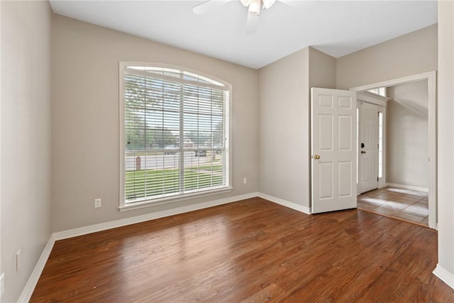 empty room with healthy amount of natural light, wood finished floors, ceiling fan, and baseboards