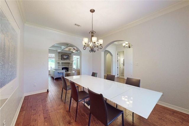 dining area featuring a fireplace, an inviting chandelier, dark wood-type flooring, and crown molding