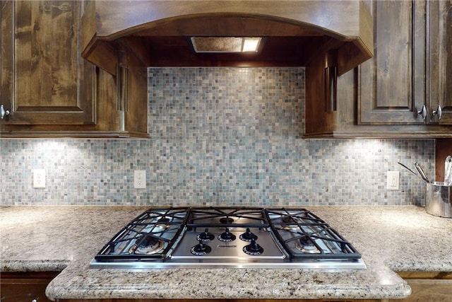 kitchen featuring tasteful backsplash, light stone countertops, custom range hood, and stainless steel gas cooktop