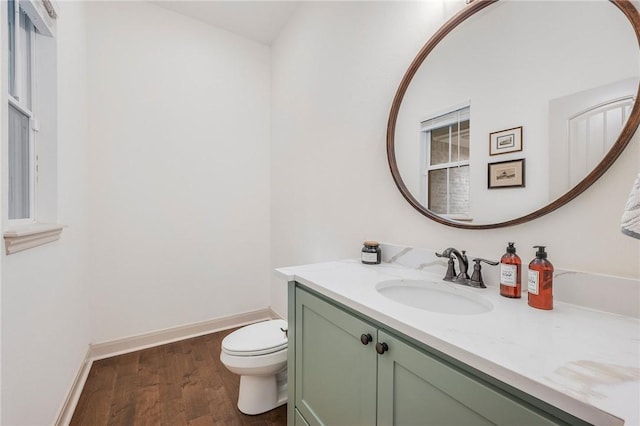 half bathroom with toilet, baseboards, wood finished floors, and vanity