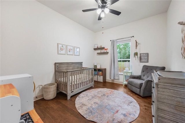 bedroom with dark wood-style floors, ceiling fan, a crib, and baseboards