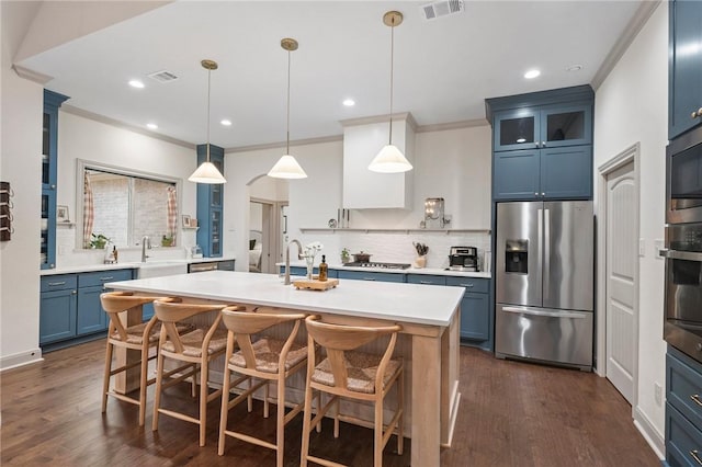 kitchen featuring decorative light fixtures, a center island with sink, light countertops, appliances with stainless steel finishes, and glass insert cabinets