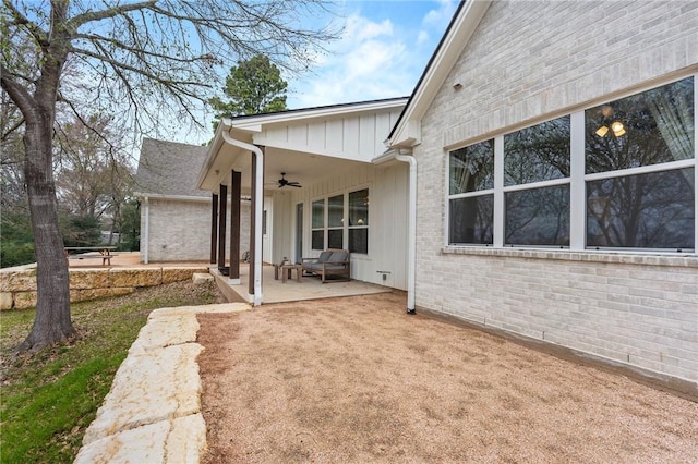 exterior space featuring a patio, brick siding, board and batten siding, and a ceiling fan