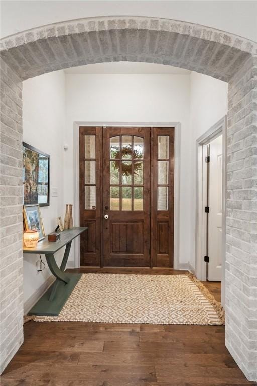 foyer entrance with arched walkways, brick wall, and dark wood finished floors