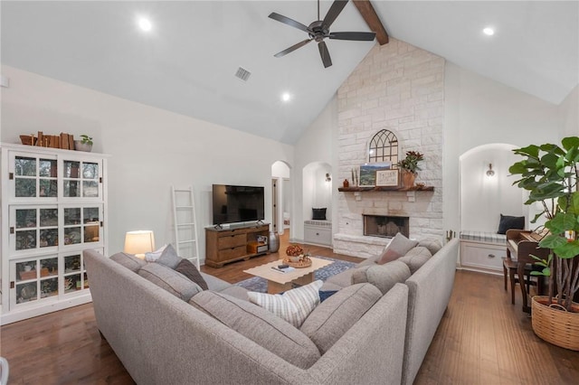 living area with arched walkways, visible vents, a stone fireplace, wood finished floors, and beamed ceiling