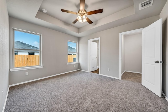 unfurnished bedroom with dark colored carpet, a raised ceiling, and ceiling fan