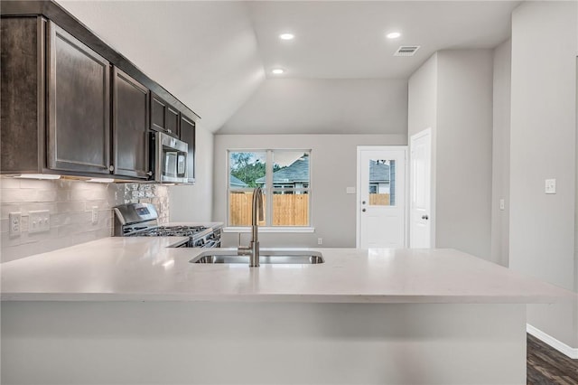 kitchen featuring dark brown cabinetry, sink, stainless steel appliances, kitchen peninsula, and vaulted ceiling