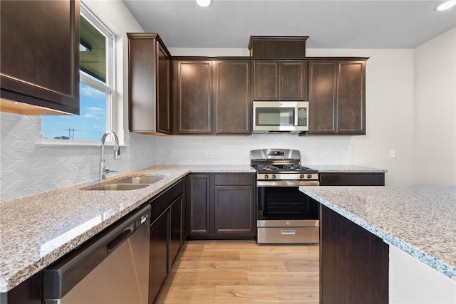 kitchen with dark brown cabinetry, light stone countertops, sink, appliances with stainless steel finishes, and light wood-type flooring