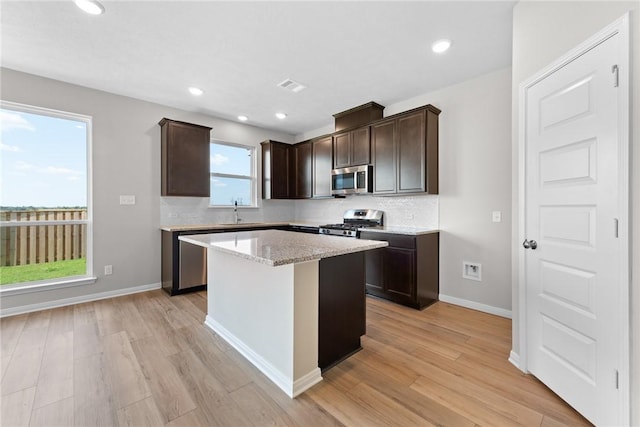 kitchen featuring light stone counters, light hardwood / wood-style floors, dark brown cabinets, a kitchen island, and appliances with stainless steel finishes