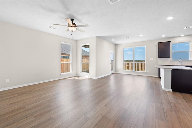 unfurnished living room with ceiling fan, sink, and light hardwood / wood-style flooring