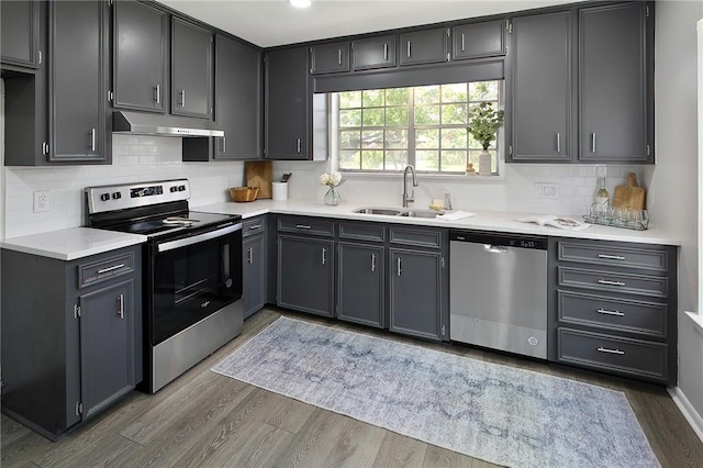 kitchen featuring light countertops, under cabinet range hood, stainless steel appliances, a sink, and wood finished floors