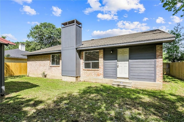 rear view of house featuring a yard, fence private yard, brick siding, a chimney, and a shingled roof