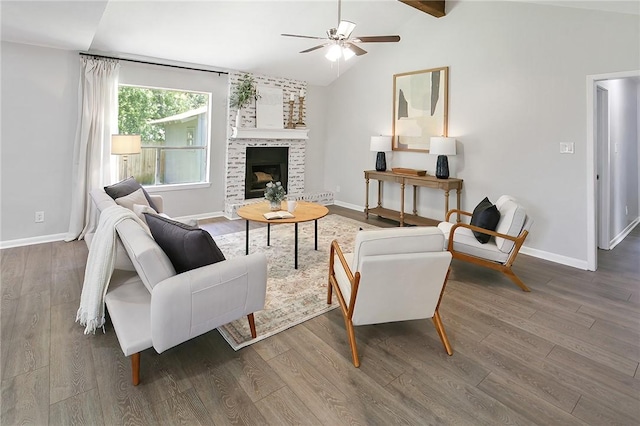 living room featuring baseboards, lofted ceiling with beams, a brick fireplace, ceiling fan, and wood finished floors