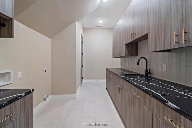 kitchen with dark stone counters, sink, vaulted ceiling, light tile patterned floors, and tasteful backsplash