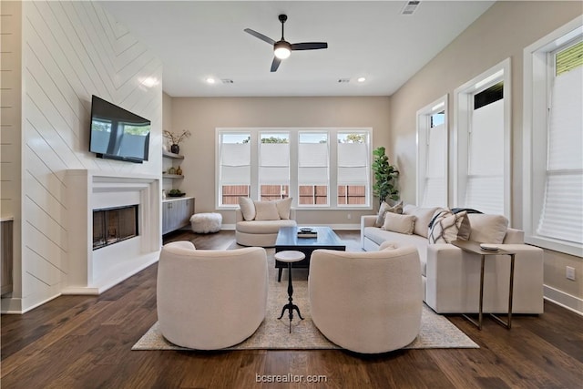 living room featuring dark hardwood / wood-style floors, a large fireplace, and ceiling fan