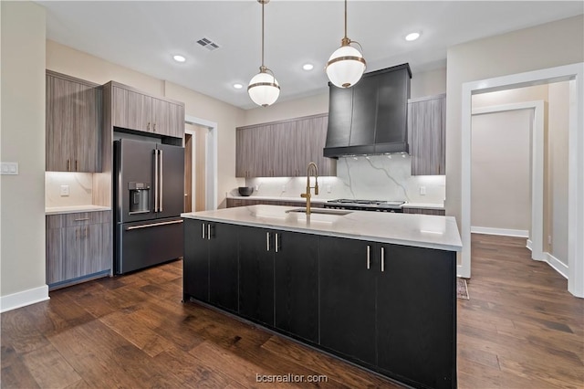 kitchen featuring custom exhaust hood, a center island with sink, sink, decorative light fixtures, and high end fridge