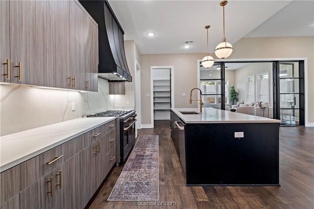 kitchen featuring sink, hanging light fixtures, stainless steel appliances, dark hardwood / wood-style flooring, and a center island with sink