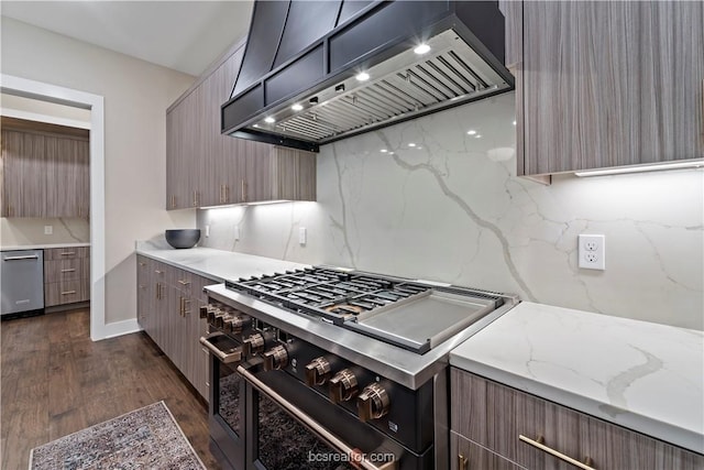 kitchen featuring light stone countertops, dark wood-type flooring, premium range hood, decorative backsplash, and appliances with stainless steel finishes