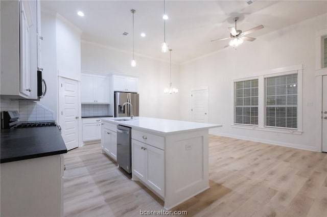 kitchen featuring pendant lighting, white cabinets, ceiling fan with notable chandelier, an island with sink, and tasteful backsplash