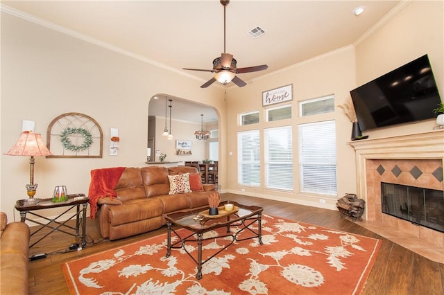 living room featuring ceiling fan, wood-type flooring, ornamental molding, and a tiled fireplace