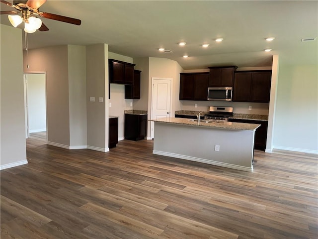 kitchen with hardwood / wood-style floors, a kitchen island with sink, light stone countertops, dark brown cabinets, and stainless steel appliances