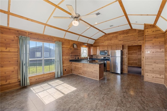 kitchen with high vaulted ceiling, dark countertops, stainless steel appliances, a peninsula, and wood walls