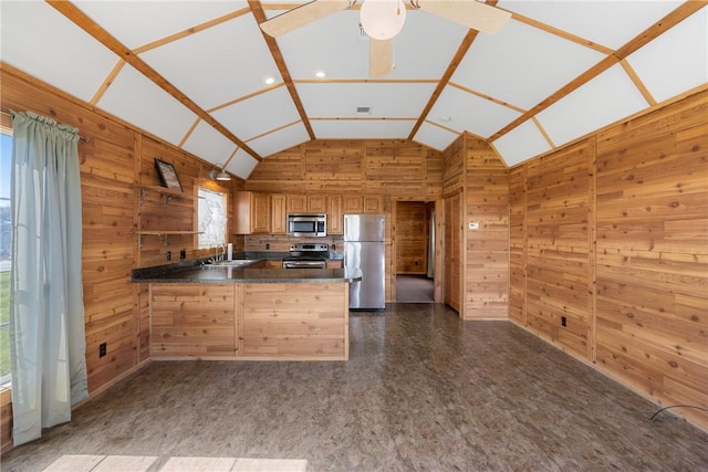 kitchen with a sink, dark countertops, stainless steel appliances, a peninsula, and wood walls