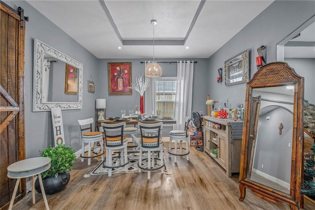 dining space with a barn door, light wood-type flooring, and a tray ceiling