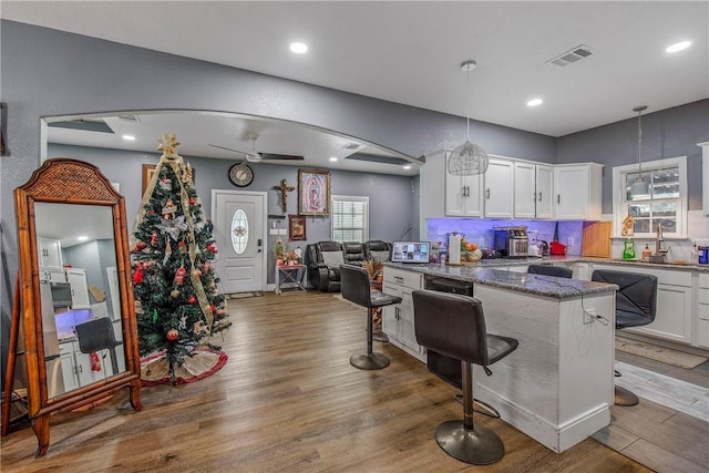 kitchen with dark stone countertops, decorative light fixtures, a breakfast bar, and white cabinets