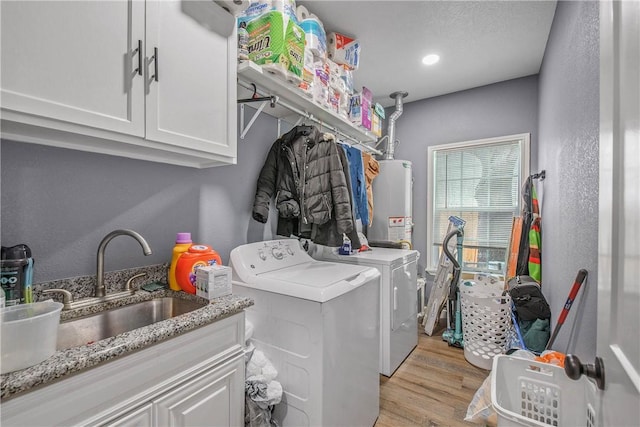 laundry room featuring sink, light hardwood / wood-style flooring, water heater, cabinets, and separate washer and dryer