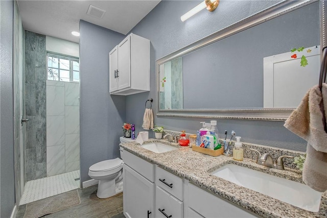 bathroom with hardwood / wood-style floors, vanity, a tile shower, and toilet