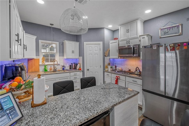 kitchen with white cabinetry, sink, hanging light fixtures, light stone counters, and stainless steel appliances