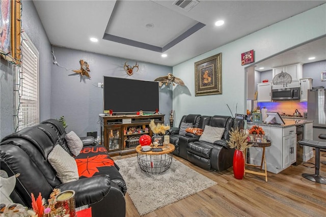 living room with a tray ceiling and light hardwood / wood-style flooring